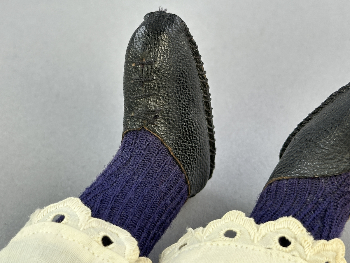 Docka klädd i kvinnlig sockendräkt föreställande Jösse härad i Värmland (hätta från Brunskog). Huvud och händer sydda av sämskskinn samt kropp av satin-tyg.