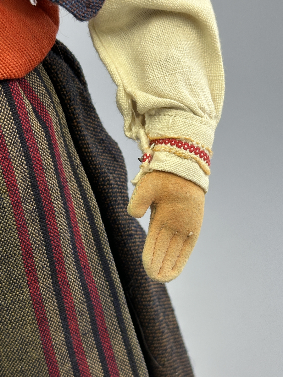 Docka klädd i kvinnlig sockendräkt föreställande Ekshärads socken i Värmland. Huvud och händer sydda av sämskskinn samt kropp av trikåtyg.
