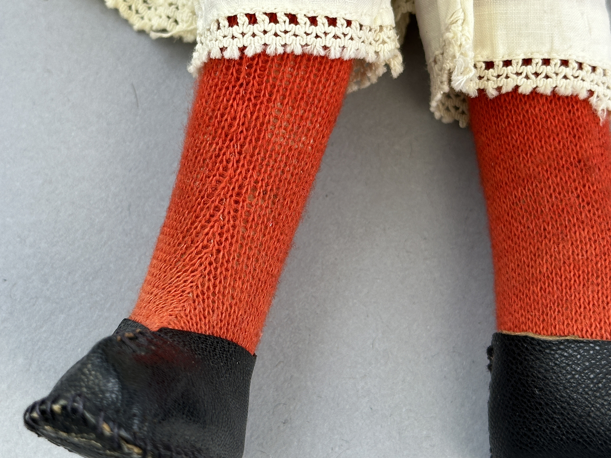 Docka klädd i kvinnlig sockendräkt föreställande Ekshärads socken i Värmland. Huvud och händer sydda av sämskskinn samt kropp av trikåtyg.
