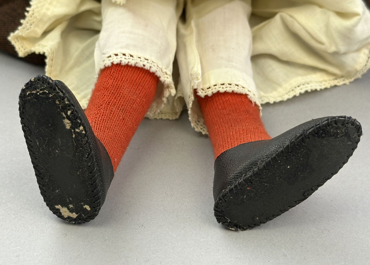Docka klädd i kvinnlig sockendräkt föreställande Ekshärads socken i Värmland. Huvud och händer sydda av sämskskinn samt kropp av trikåtyg.
