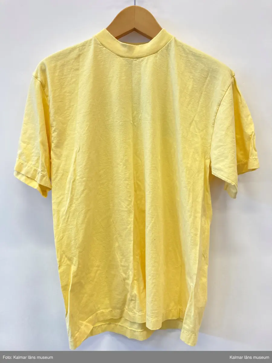 KLM 46894:3. T-shirt. Av bomull i gult med tryckt på ryggen i blått, rött och gult med text: Salve. Storlek large.