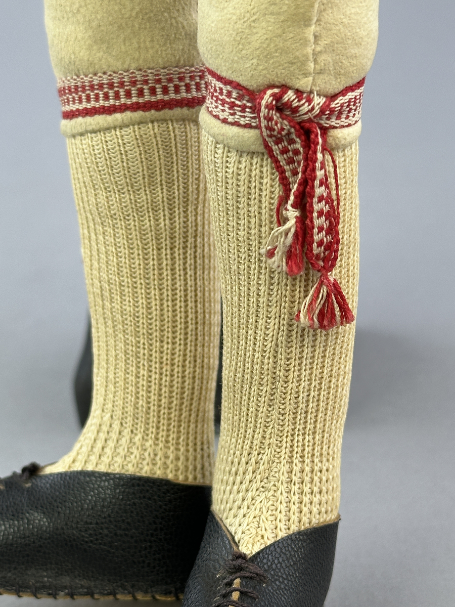 Docka klädd i manlig sockendräkt föreställande Östervallskogs socken i Värmland. Huvud och händer sydda av sämskskinn samt kropp av linnetyg.