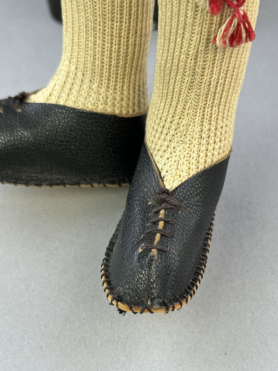 Docka klädd i manlig sockendräkt föreställande Östervallskogs socken i Värmland. Huvud och händer sydda av sämskskinn samt kropp av linnetyg.