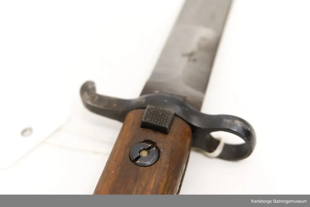Bajonett m/1914, för karbin m/1894-1914. Bajonett är ett blankvapen som fästs vid mynningen på musköter, gevär eller karbiner och som används i närstrid. Karbin m/1894-1914 saknade ursprungligen bajonett, men försågs år 1914 med sådan. Märkt EJ AB (Eskilstuna Jernmanufaktur AB). Bajonettens balja saknas. Handtag av metall och trä.