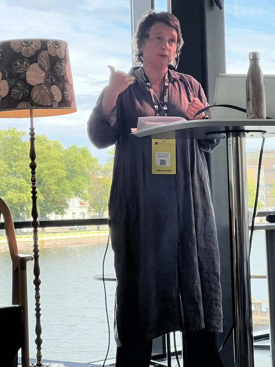 En kvinne står og snakker ved et høyt bord