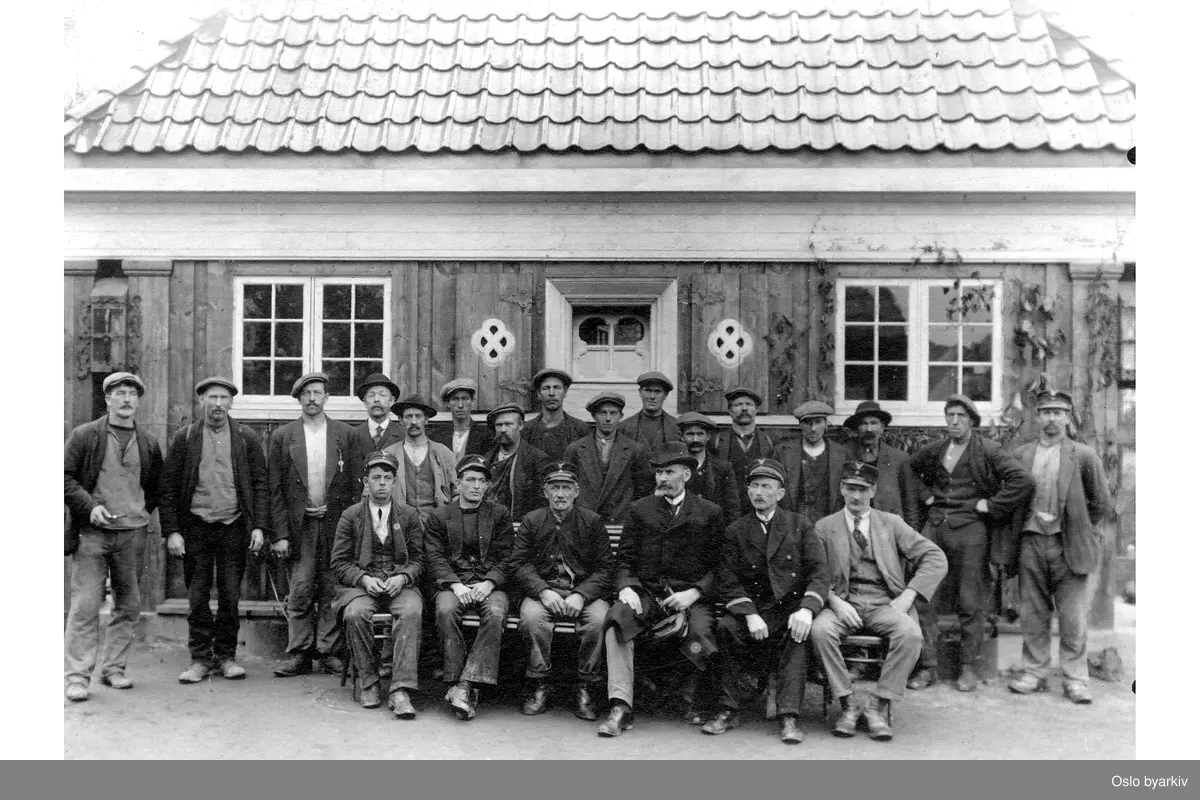 Personalbilde av arbeidere foran trehus.
