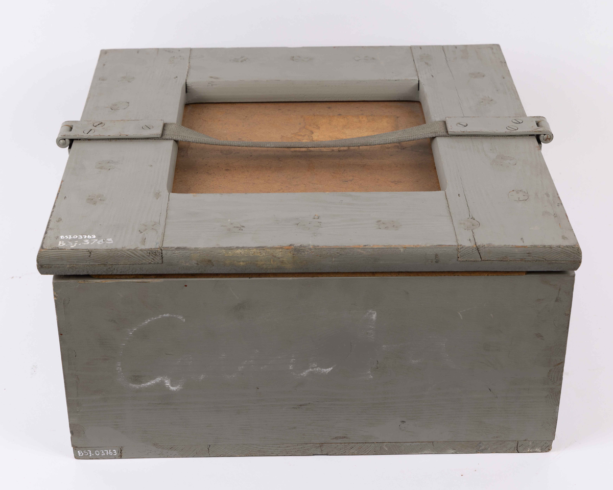 Spritkompass i gråmalt transportkasse av tre. Beregnet til bruk ombord på MS COMETA til BDS. Firkantet transportkasse med løst lokk festet til kasse med hengsel og skinnreim. Lokk med til sammen 20 runde pinner for å holde kompass på plass under transport.