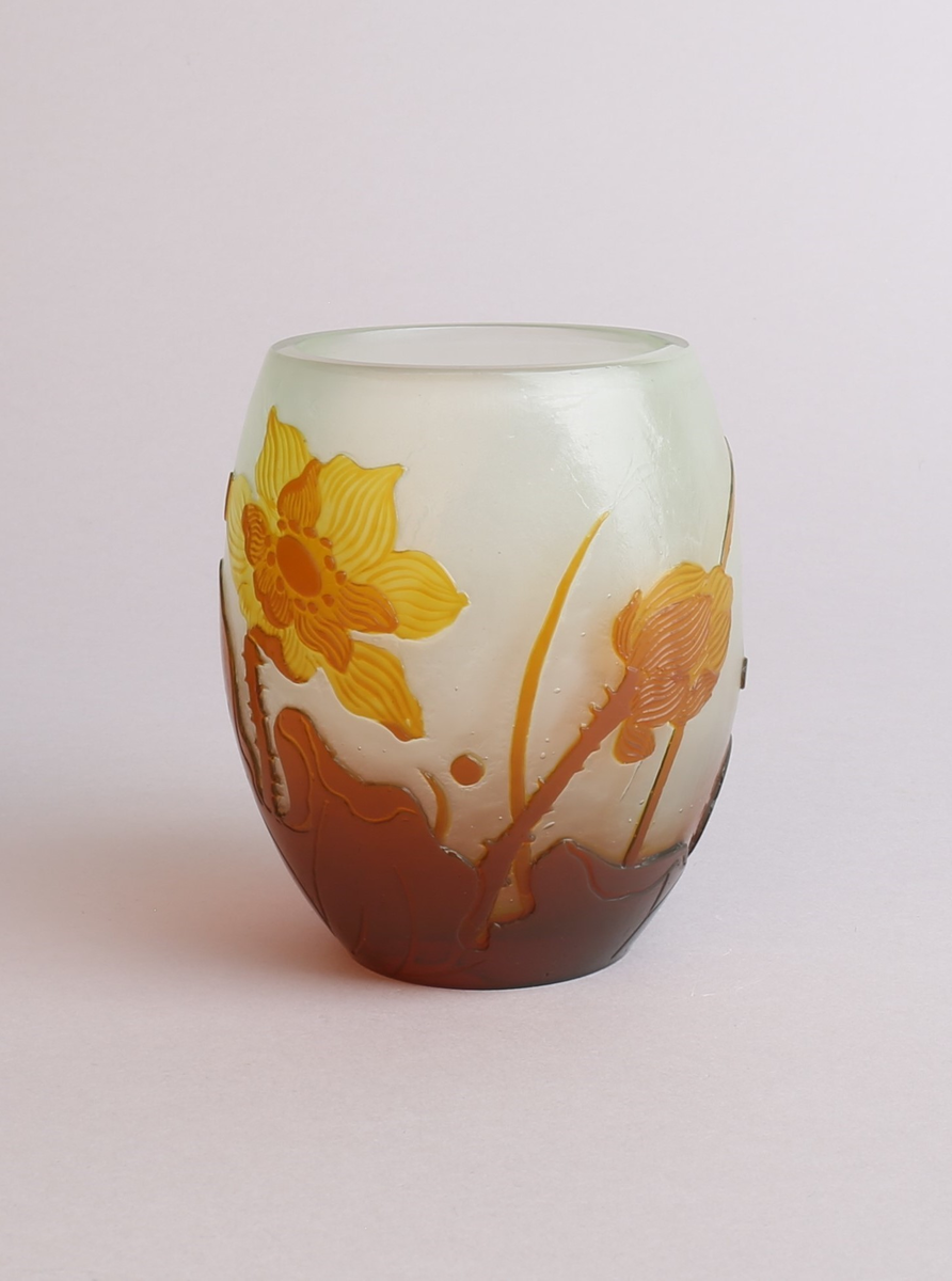 Vase med lokk i melkehvitt opakt overfangsglass. Eggeformet korpus som er dekorert med en gul blomst samt brunlig bladverk i overfangsteknikk. Deler av overflaten er trolig etset.