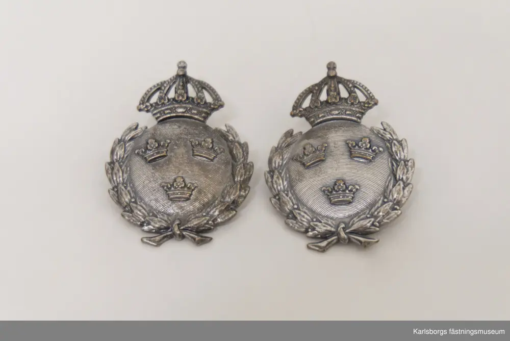 Två fältidrottsmärken i silver, ej äkta silver, med Sveriges lilla riksvapen bestående av tre kronor i en krönt cirkel. Motivet omges av en lagerkrans.  På deras baksidor är dem märkta SPORRONG.