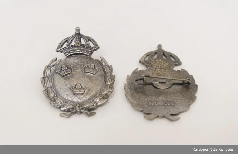 Två fältidrottsmärken i silver, ej äkta silver, med Sveriges lilla riksvapen bestående av tre kronor i en krönt cirkel. Motivet omges av en lagerkrans.  På deras baksidor är dem märkta SPORRONG.