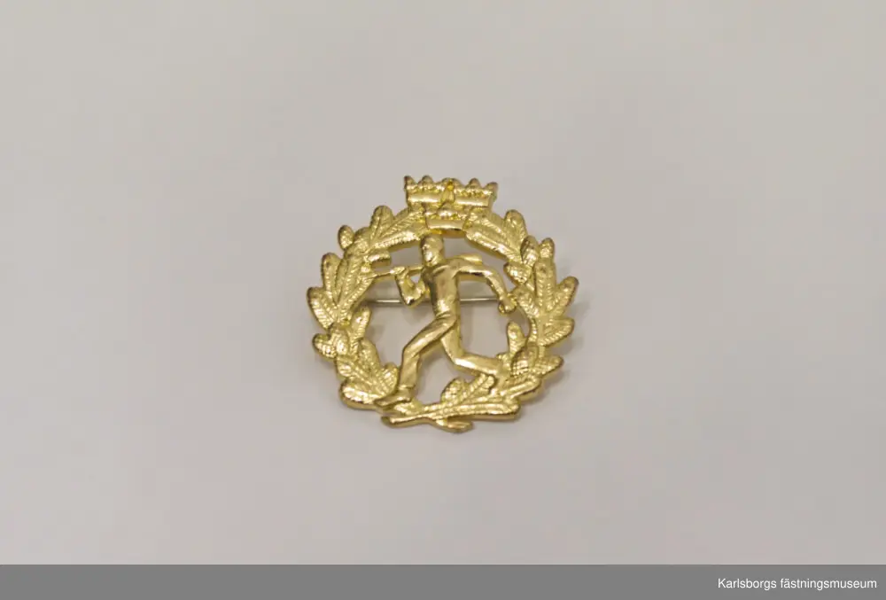 Tvågrensmärket i silver, två stycken, och en i guld. Fäste med nål på baksidan. Tvågrensmärket innebär att springa ett par kilometer och därefter skjuta på skjutbana. Diameter: ca 25mm.