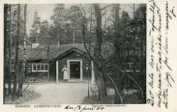 Brevkort adresserat till sjuksköterskan Amanda Palm.
Motiv av Laxbrostugan på Skansen med en kvinna i hembygdsdräkt utanför.
Text på framsidan: "den13 juni 05. Det hela har varit ofantligt intressant och icke minst detta. Jag far hem imorgon. J".