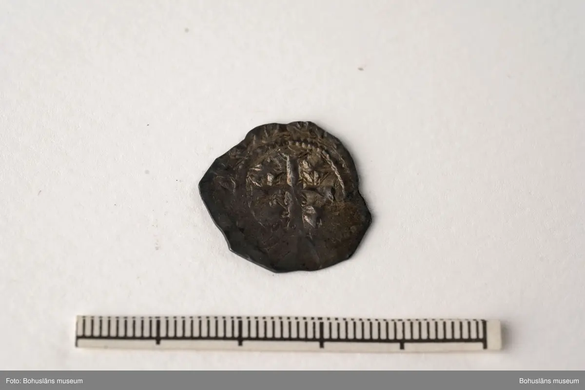 Silvermynt, England Henry II (1154-89), penny 1158-80. North 956-70 var; SCBI 12 Oxford 301 ff, 'Cross and crosslets'-typ. 
Vikt: 1,385 g.

Bro kastal i Bro socken, Lysekils kommun byggdes under 1110-talet. Kastalen bestod av ett kraftigt fristående torn, uppfört uppe på en kulle och var en tidig typ av borganläggning. Från kastalen hade man milsvid utsikt över den omgivande trakten.
Kastalens grund mäter en fyrkant om 8,7 x 8,4 meter. Invändigt har funnits valvslaget tak och halvmeterbreda inre gångar. Tornets ursprungliga höjd bedöms till 10 meter.
Fynden från arkeologiska undersökningar på 1960- och 1970-talen visar att kastalen varit i bruk från 1100-talet fram till början av 1400-talet. 
Tre mynt daterar kastalen; en engelsk silverpenny från andra halvan av 1100-talet, ett mynt från antingen kung Sverres (1176 -1202) eller sonen  Håkon Håkonssons regering samt ett fragmentariskt mynt från perioden 1160-1205, av okänt ursprung. 
Mycket i fyndmaterialet ger en koppling till samhällets övre skikt, bl.a. en guldring, en piksporre, en nöt (del till ett armborst) och en stjärntrissa till en sporre. 
Bland benfynden finns rester av duvhök som kan ha varit dresserad för jakt. 
Till vapenfynden hör en stridsyxa av järn från 1100-talet och fyra pilspetsar. 
En del bruksföremål som brynen, en kläppkrok som användes vid havsfiske och en ljusterudd tyder på att borgen varit bebodd åtminstone tidvis (se Pettersson, J. 1987).