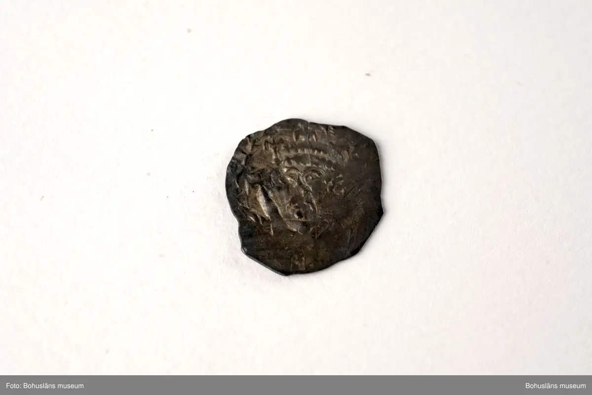 Silvermynt, England Henry II (1154-89), penny 1158-80. North 956-70 var; SCBI 12 Oxford 301 ff, 'Cross and crosslets'-typ. 
Vikt: 1,385 g.

Bro kastal i Bro socken, Lysekils kommun byggdes under 1110-talet. Kastalen bestod av ett kraftigt fristående torn, uppfört uppe på en kulle och var en tidig typ av borganläggning. Från kastalen hade man milsvid utsikt över den omgivande trakten.
Kastalens grund mäter en fyrkant om 8,7 x 8,4 meter. Invändigt har funnits valvslaget tak och halvmeterbreda inre gångar. Tornets ursprungliga höjd bedöms till 10 meter.
Fynden från arkeologiska undersökningar på 1960- och 1970-talen visar att kastalen varit i bruk från 1100-talet fram till början av 1400-talet. 
Tre mynt daterar kastalen; en engelsk silverpenny från andra halvan av 1100-talet, ett mynt från antingen kung Sverres (1176 -1202) eller sonen  Håkon Håkonssons regering samt ett fragmentariskt mynt från perioden 1160-1205, av okänt ursprung. 
Mycket i fyndmaterialet ger en koppling till samhällets övre skikt, bl.a. en guldring, en piksporre, en nöt (del till ett armborst) och en stjärntrissa till en sporre. 
Bland benfynden finns rester av duvhök som kan ha varit dresserad för jakt. 
Till vapenfynden hör en stridsyxa av järn från 1100-talet och fyra pilspetsar. 
En del bruksföremål som brynen, en kläppkrok som användes vid havsfiske och en ljusterudd tyder på att borgen varit bebodd åtminstone tidvis (se Pettersson, J. 1987).