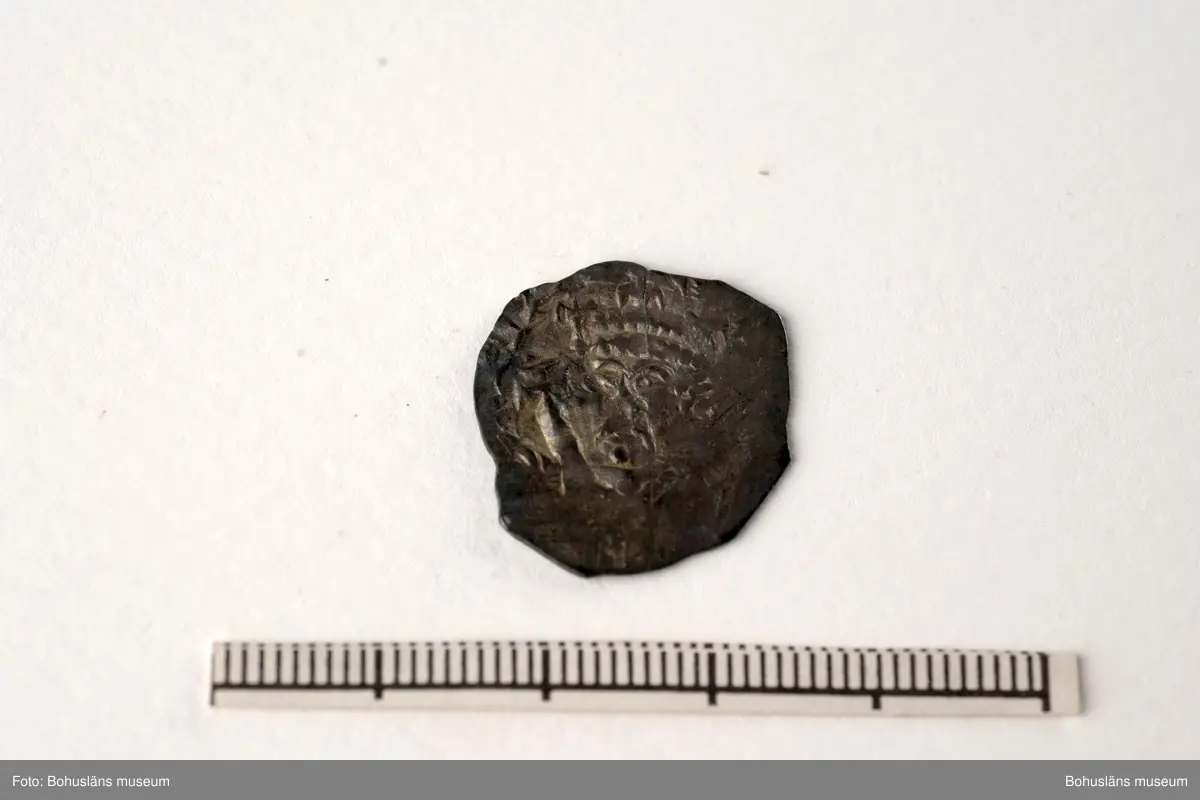 Silvermynt, England Henry II (1154-89), penny 1158-80. North 956-70 var; SCBI 12 Oxford 301 ff, 'Cross and crosslets'-typ. 
Vikt: 1,385 g.

Bro kastal i Bro socken, Lysekils kommun byggdes under 1110-talet. Kastalen bestod av ett kraftigt fristående torn, uppfört uppe på en kulle och var en tidig typ av borganläggning. Från kastalen hade man milsvid utsikt över den omgivande trakten.
Kastalens grund mäter en fyrkant om 8,7 x 8,4 meter. Invändigt har funnits valvslaget tak och halvmeterbreda inre gångar. Tornets ursprungliga höjd bedöms till 10 meter.
Fynden från arkeologiska undersökningar på 1960- och 1970-talen visar att kastalen varit i bruk från 1100-talet fram till början av 1400-talet. 
Tre mynt daterar kastalen; en engelsk silverpenny från andra halvan av 1100-talet, ett mynt från antingen kung Sverres (1176 -1202) eller sonen  Håkon Håkonssons regering samt ett fragmentariskt mynt från perioden 1160-1205, av okänt ursprung. 
Mycket i fyndmaterialet ger en koppling till samhällets övre skikt, bl.a. en guldring, en piksporre, en nöt (del till ett armborst) och en stjärntrissa till en sporre. 
Bland benfynden finns rester av duvhök som kan ha varit dresserad för jakt. 
Till vapenfynden hör en stridsyxa av järn från 1100-talet och fyra pilspetsar. 
En del bruksföremål som brynen, en kläppkrok som användes vid havsfiske och en ljusterudd tyder på att borgen varit bebodd åtminstone tidvis (se Pettersson, J. 1987).
