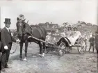 En vagn, dekorerad med pappersblommor.  I vagnen sitter tre blomsterflickor.
En man i kostym och hög hatt håller hästen framför.