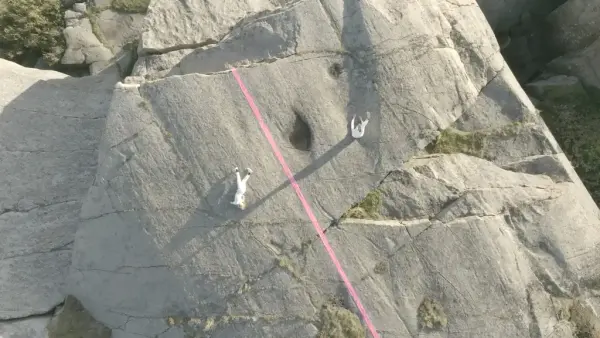 Viser to hvitkledde personer fremføre koreografi, mens de henger i en fjellvegg.