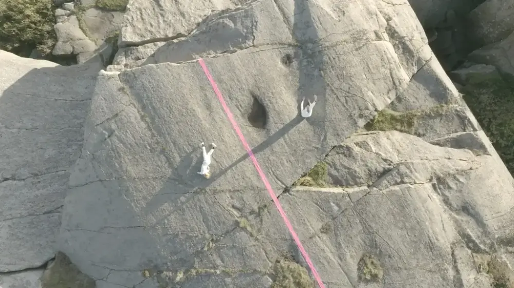 Viser to hvitkledde personer fremføre koreografi, mens de henger i en fjellvegg.