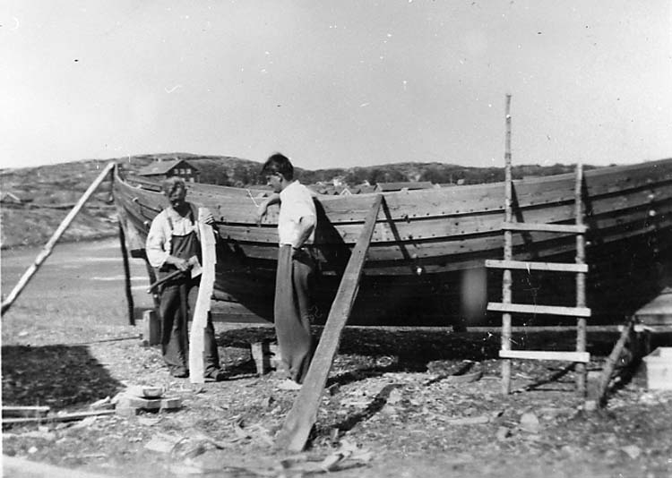Medföljande text: "Koster. Till vänster båtbyggare Carl Johan Hansson som hugger till spant, till höger en badgäst. Bilden tagen på 1950-talet. 
Originalfoto tillhörande Carl Johan Hansson, Koster".