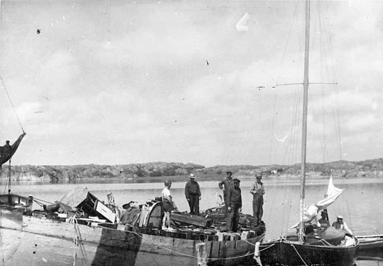 Medföljande text: "Carl och Gustav Olssons varv i Bovallstrand. Reparationsarbeten på fiskebåt. (samma fiskebåt som på bild R.67:2). Övre bordgången borttagen. På fiskebåten syns fr v sommargästbarn (Sundkvist), Mauritz Mattsson. okänd, Carl Olsson och Birger Tillander. Till höger i bild syns kosterbåt med sommargäster. Bilden tagen under andra världskriget. Originalfoto tillhörande Gustav Olsson, Smögen".