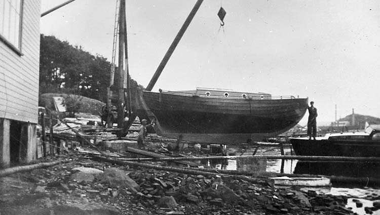 Medföljande text: "Nilssons Båtbyggeri, i Strömstad. Kosterbåt i kranen. Till vänster i bild syns nya verkstaden (byggd 1936). Bilden tagen ca 1939. Originalfoto tillhörande Nils Nilsson, Strömstad".