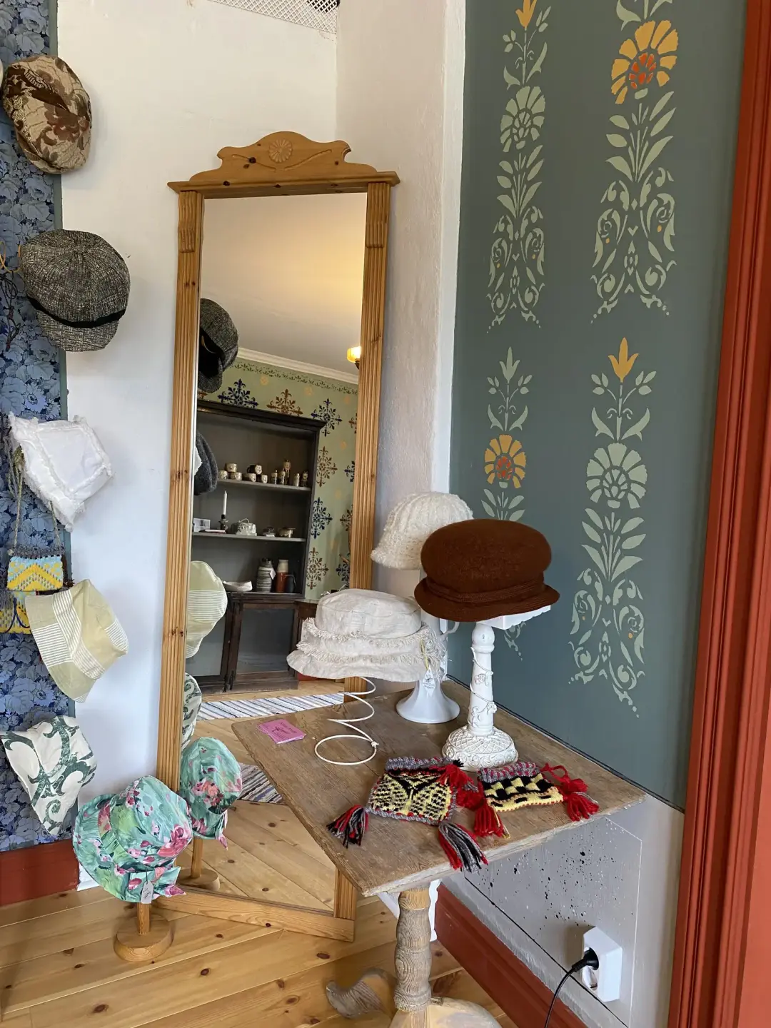 Ett hörn i ett rum. Där står en spegel och ett flertal hattar uppställda. Några hattar är på ett bord, de andra hänger från en vägg. 