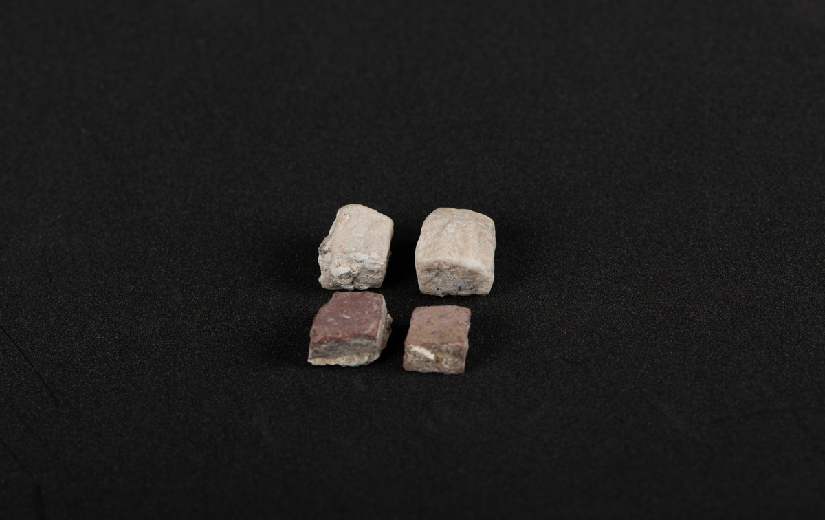Fire kvadratiske (tilnærmelsesvis) tessera. Den største med sider, på ca. 1 cm. To tesserae i hvit marmor, to i porfyr. Rester av mørtel laget på undersidene.