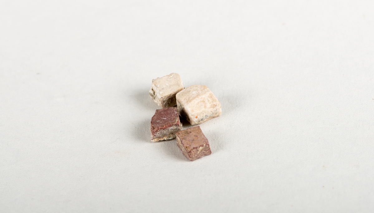 Fire kvadratiske (tilnærmelsesvis) tessera. Den største med sider, på ca. 1 cm. To tesserae i hvit marmor, to i porfyr. Rester av mørtel laget på undersidene.