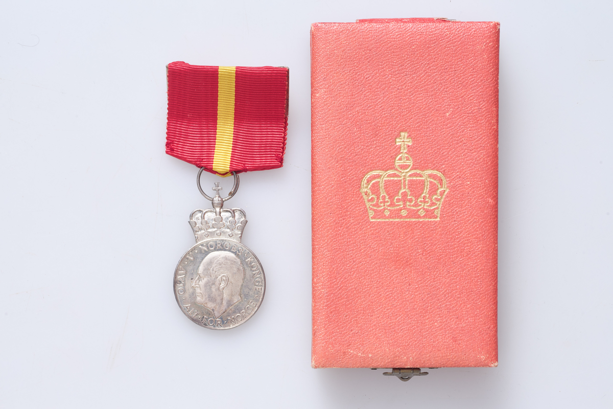 Kongens fortjenestmedalje i sølv (a) med etui (b). Medaljen er festet i et rødt og gult bånd. Tildelt Ludvig Skjerven i 1960. Etuiet dekorert med krone på lokket.