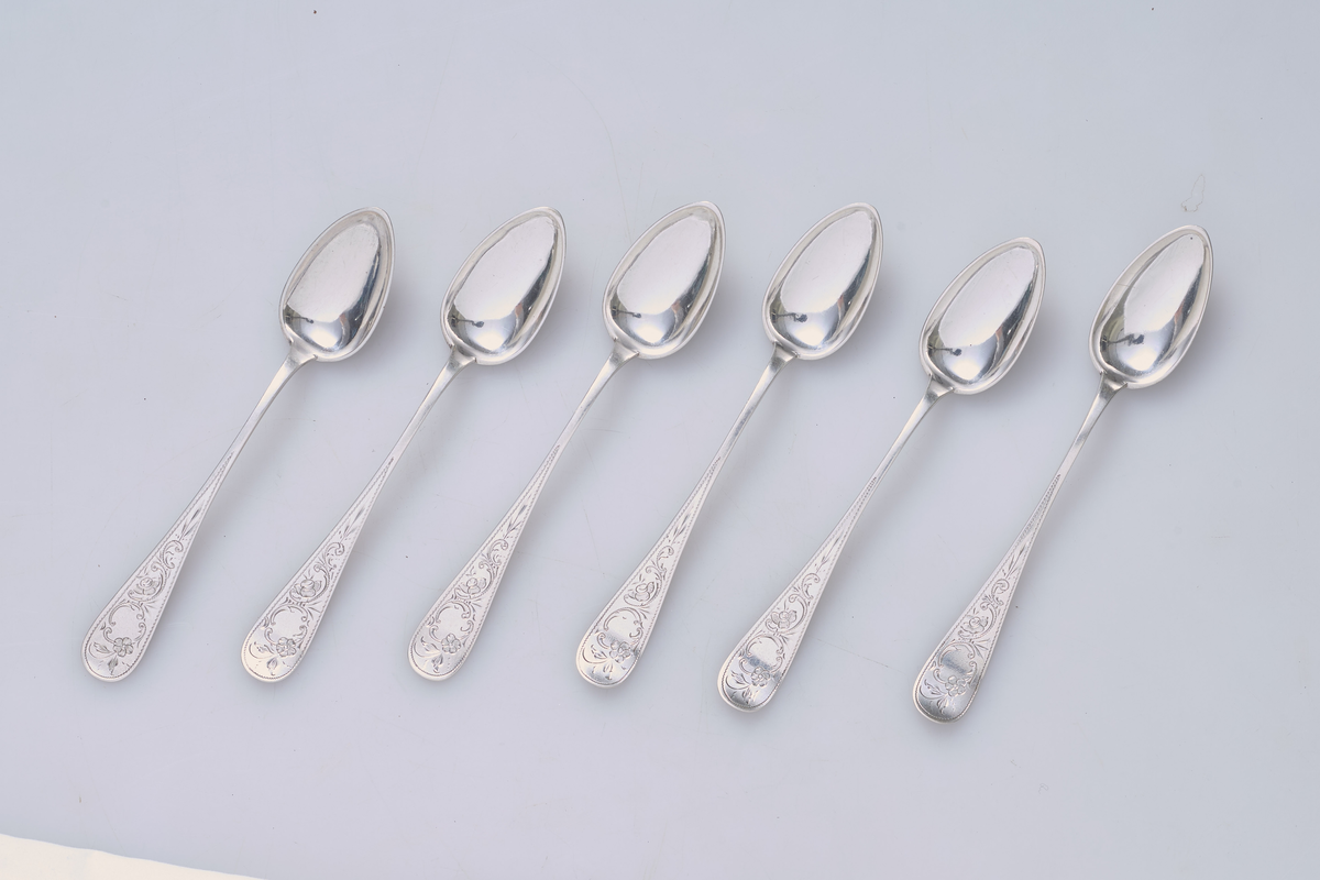Seks teskjeer i sølv med dekorert håndtak.