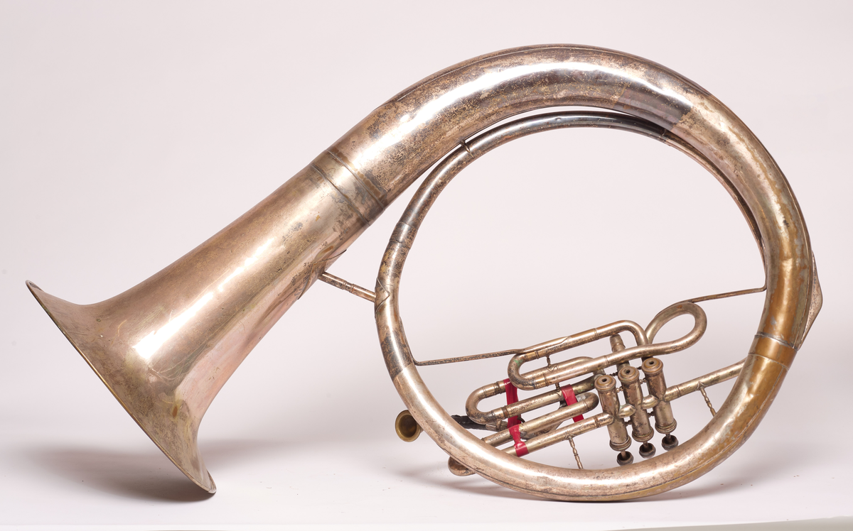 Ess-tuba produsert av Brødrene Schuster i Markneukirchen, Tyskland. Blåse - ventilinstrument. Sjalstykke med to ringer, når og tre ventiler. Bæres. Bygget i ring, rundt hals på skuldrer.