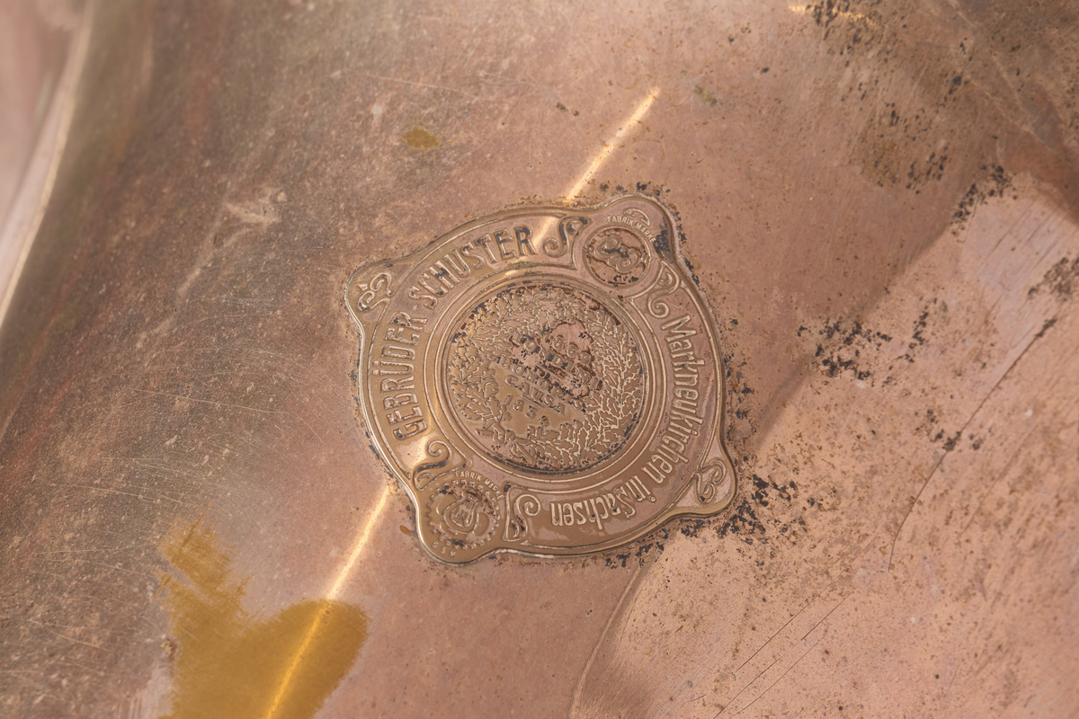 Ess-tuba produsert av Brødrene Schuster i Markneukirchen, Tyskland. Blåse - ventilinstrument. Sjalstykke med to ringer, når og tre ventiler. Bæres. Bygget i ring, rundt hals på skuldrer.