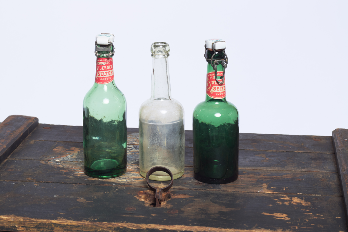 Seltersflaske med patentkork. Korken er merket med "Foss Mineralvandfabrik". Flasken er oppbevart sammen med flere andre flasker i en trekiste med lokk. På trekisten står det "Stjernens Mineralvande" på siden.