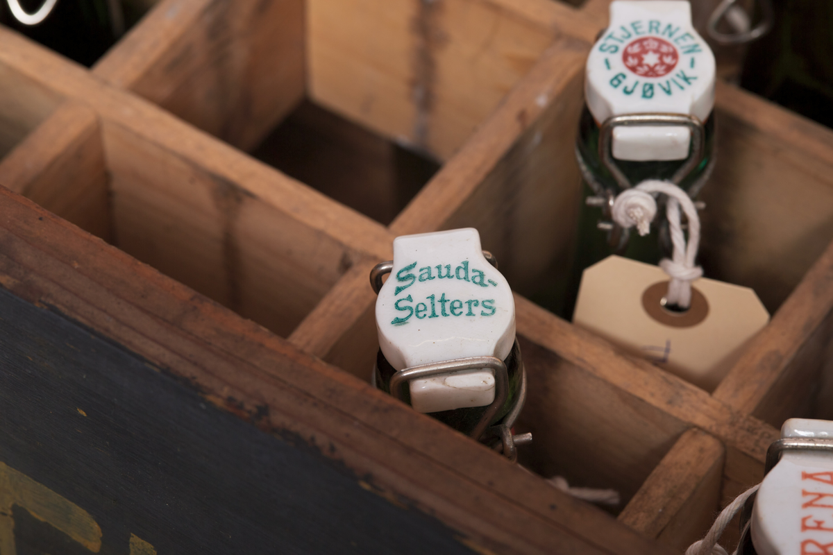 Seltersflaske med patentkork. Korken er merket med "Hortens Bryggeri". Flasken er oppbevart sammen med flere andre flasker i en trekiste med lokk. På trekisten står det "Stjernens Mineralvande" på siden.