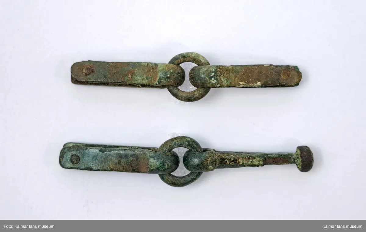 KLM 17016. Rembeslag, 2 st. Av brons. Ledade med ring i mitten.