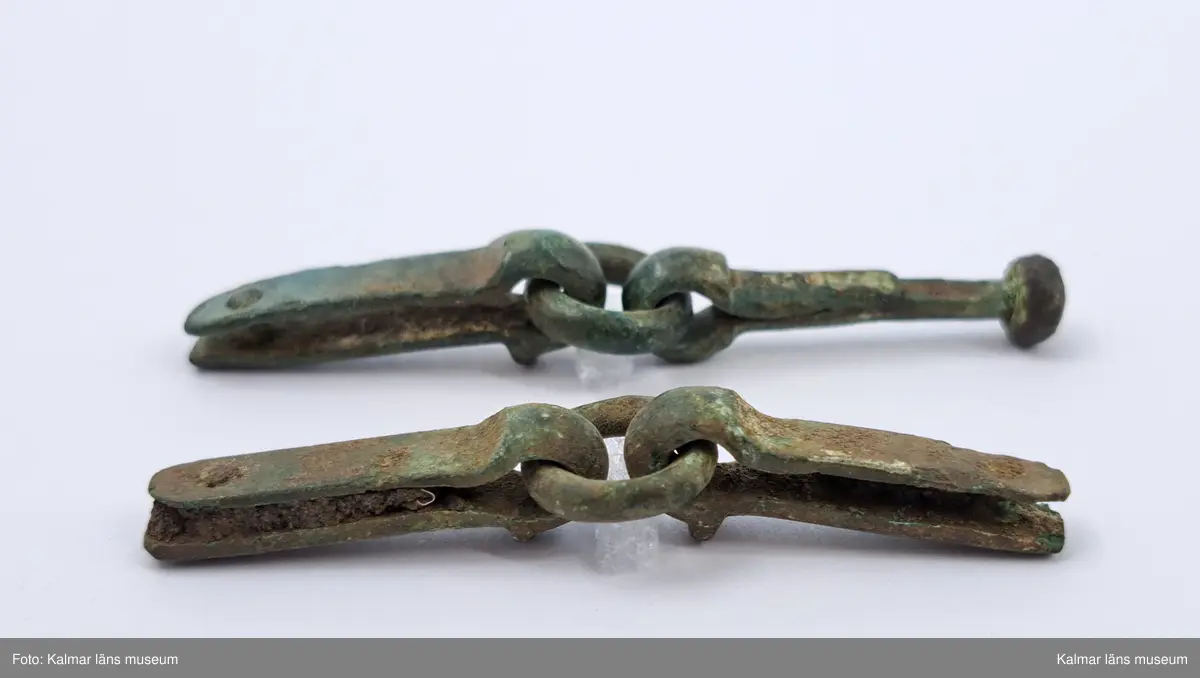 KLM 17016. Rembeslag, 2 st. Av brons. Ledade med ring i mitten.