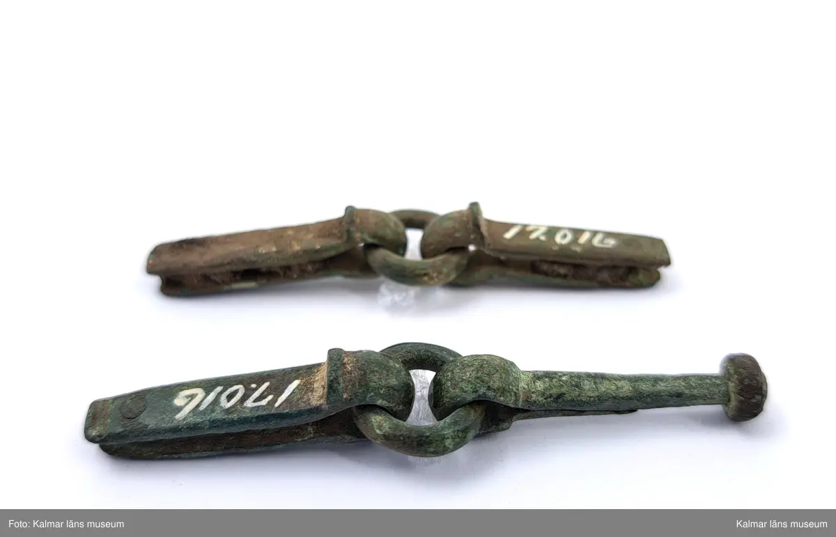 KLM 17016. Rembeslag, 2 st. Av brons. Ledade med ring i mitten.
