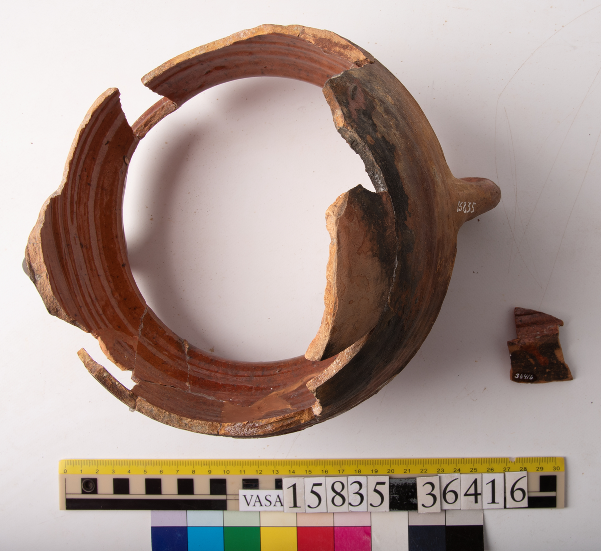 Kruka med två trindhänklar, ej komplett.
Krukan är fragmentarisk och sammansatt av ett flertal delar och bitar. Hela botten och delar av buken borta. Mynningsranden och bröstet nästan komplett. Mynningsvidd 190 mm. Förtjockad och profilerad mynningsrand med två trindhänklar som är ca 10 mm högre än mynningskanten.
På bröstet drejfåror. På skudervinkeln en ås och på bukkanten en ås.
Krukan är in- och utvändigt brunt blyglaserad, på buken mycket dåligt glaserad där den verkar sotig och sönderbränd.