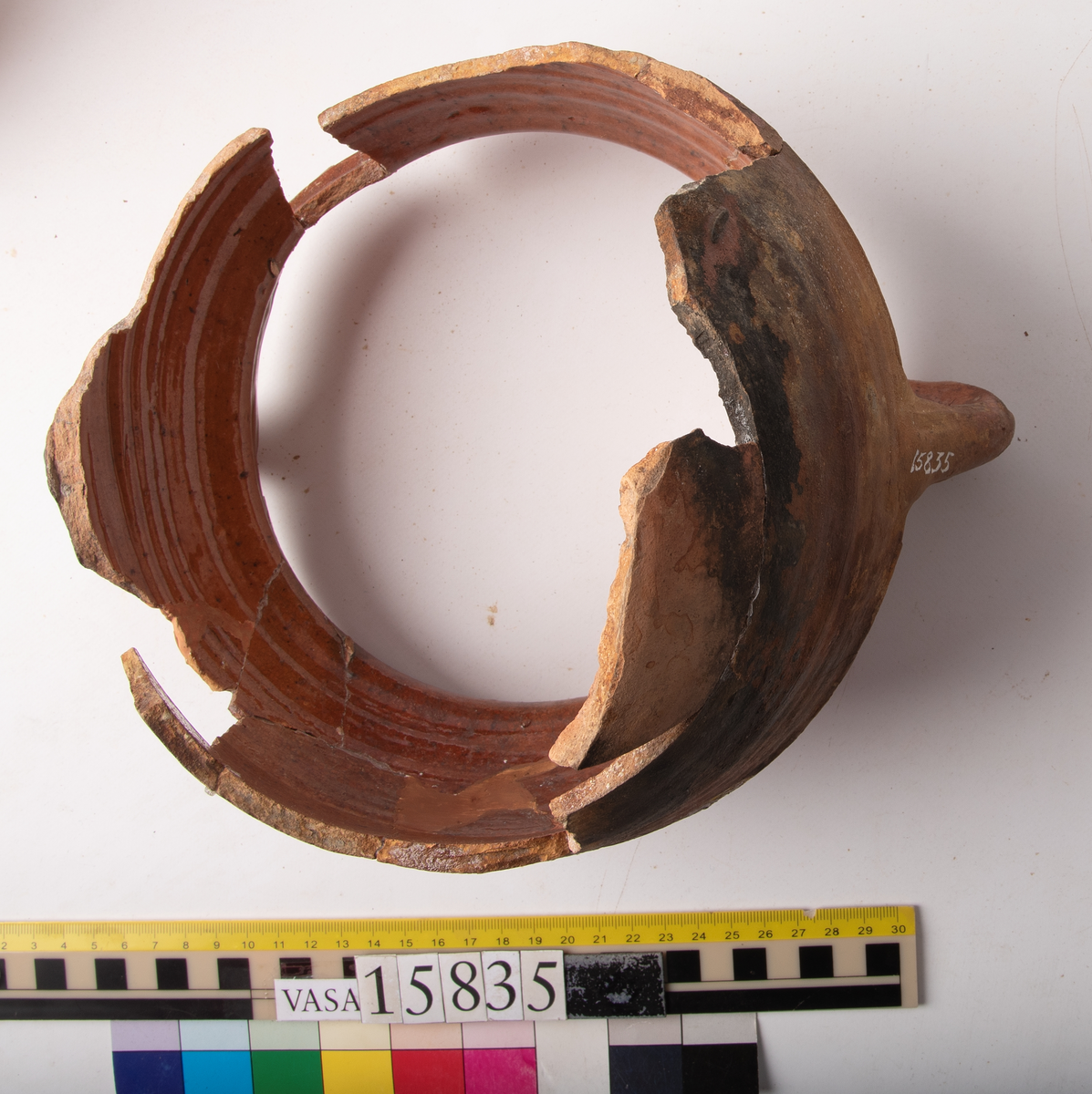 Kruka med två trindhänklar, ej komplett.
Krukan är fragmentarisk och sammansatt av ett flertal delar och bitar. Hela botten och delar av buken borta. Mynningsranden och bröstet nästan komplett. Mynningsvidd 190 mm. Förtjockad och profilerad mynningsrand med två trindhänklar som är ca 10 mm högre än mynningskanten.
På bröstet drejfåror. På skudervinkeln en ås och på bukkanten en ås.
Krukan är in- och utvändigt brunt blyglaserad, på buken mycket dåligt glaserad där den verkar sotig och sönderbränd.