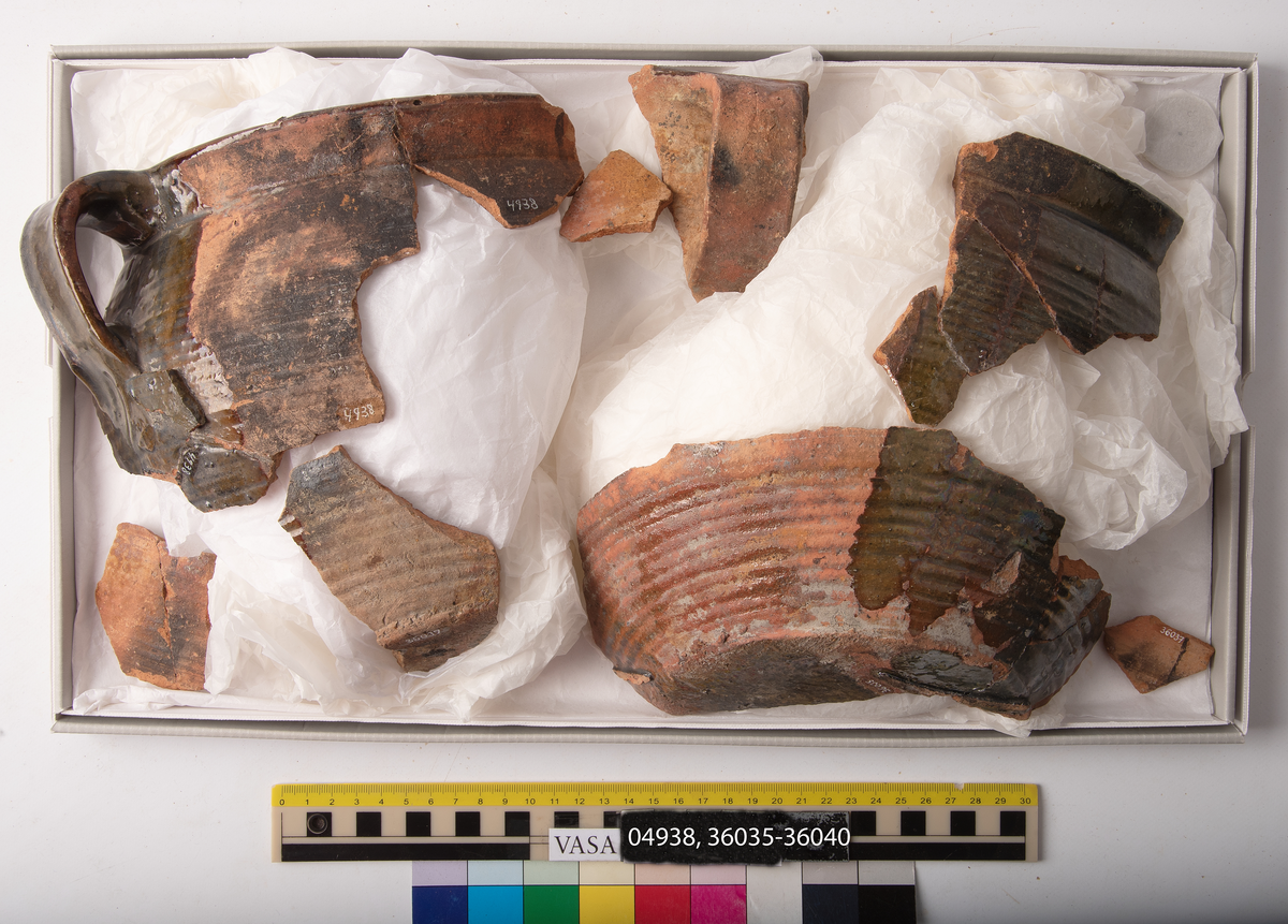 1 st bandhänkel och del av mynningsrand och skuldra. Fragment (hopsatt av 2 bitar). Insida blyglaserad brun. Utsida oglaserad.