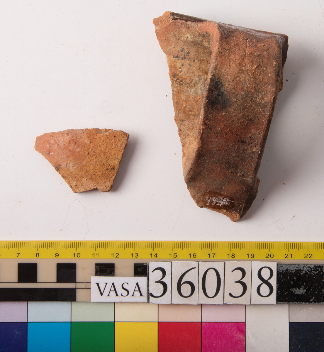 1 st bandhänkel och del av mynningsrand och skuldra. Fragment (hopsatt av 2 bitar). Insida blyglaserad brun. Utsida oglaserad.