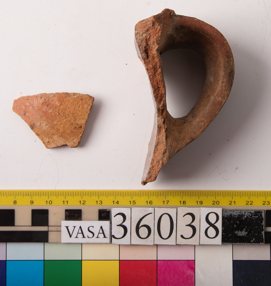 1 st bandhänkel och del av mynningsrand och skuldra. Fragment (hopsatt av 2 bitar). Insida blyglaserad brun. Utsida oglaserad.
