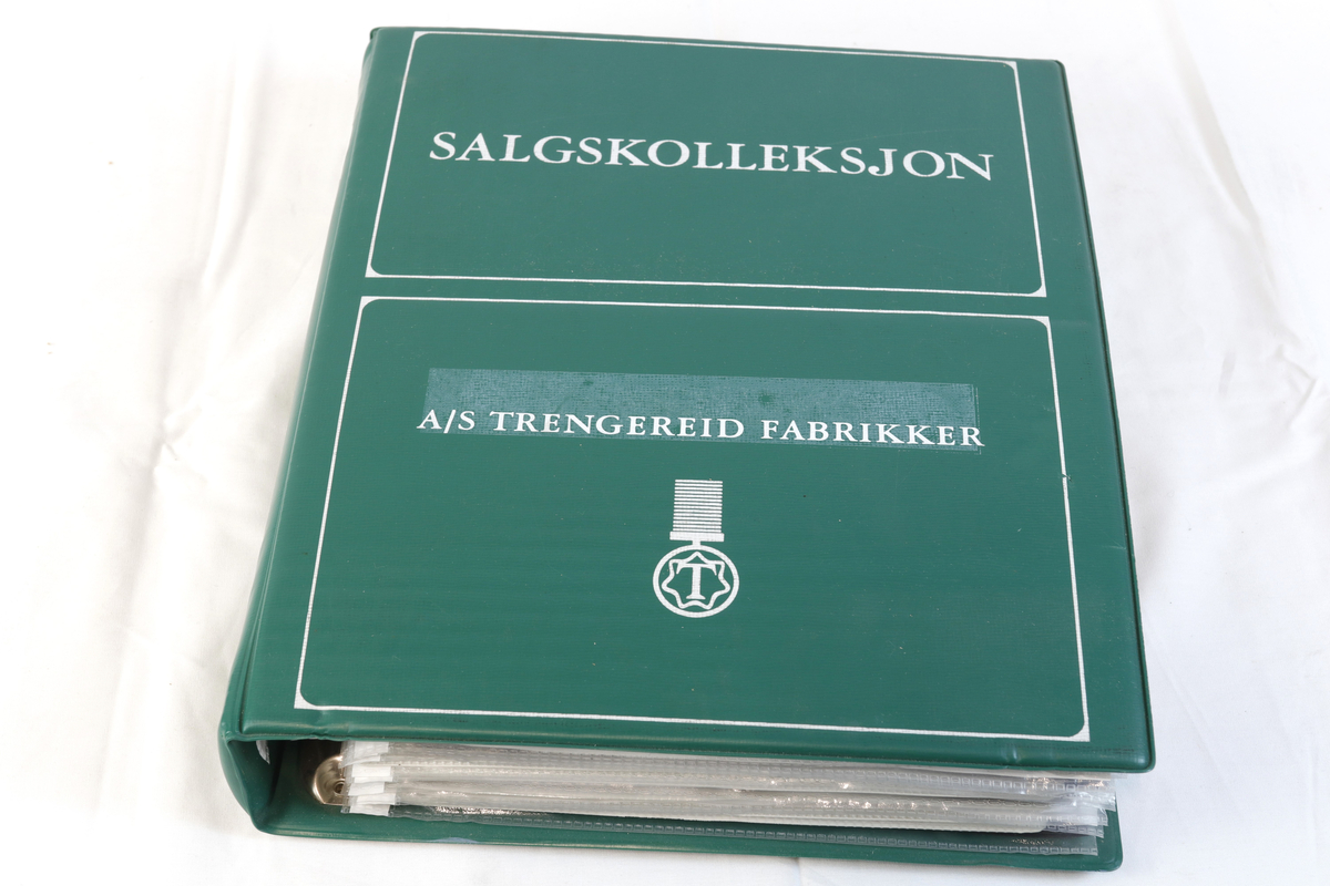 Grønn ringperm i plast. Innholder salgskolleksjon til firmaet A/S Trengreid Fabrikker.