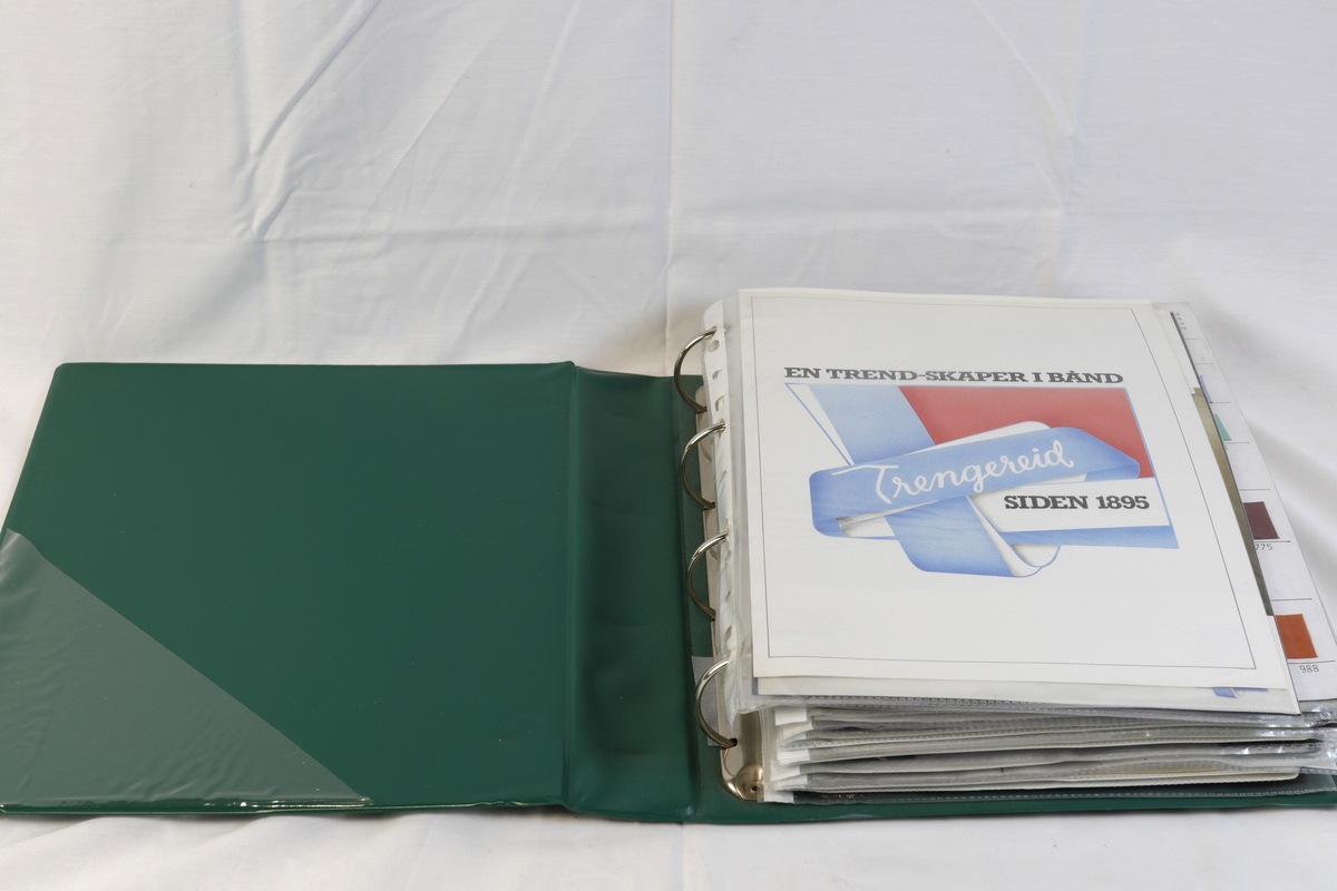 Grønn ringperm i plast. Innholder salgskolleksjon til firmaet A/S Trengreid Fabrikker.