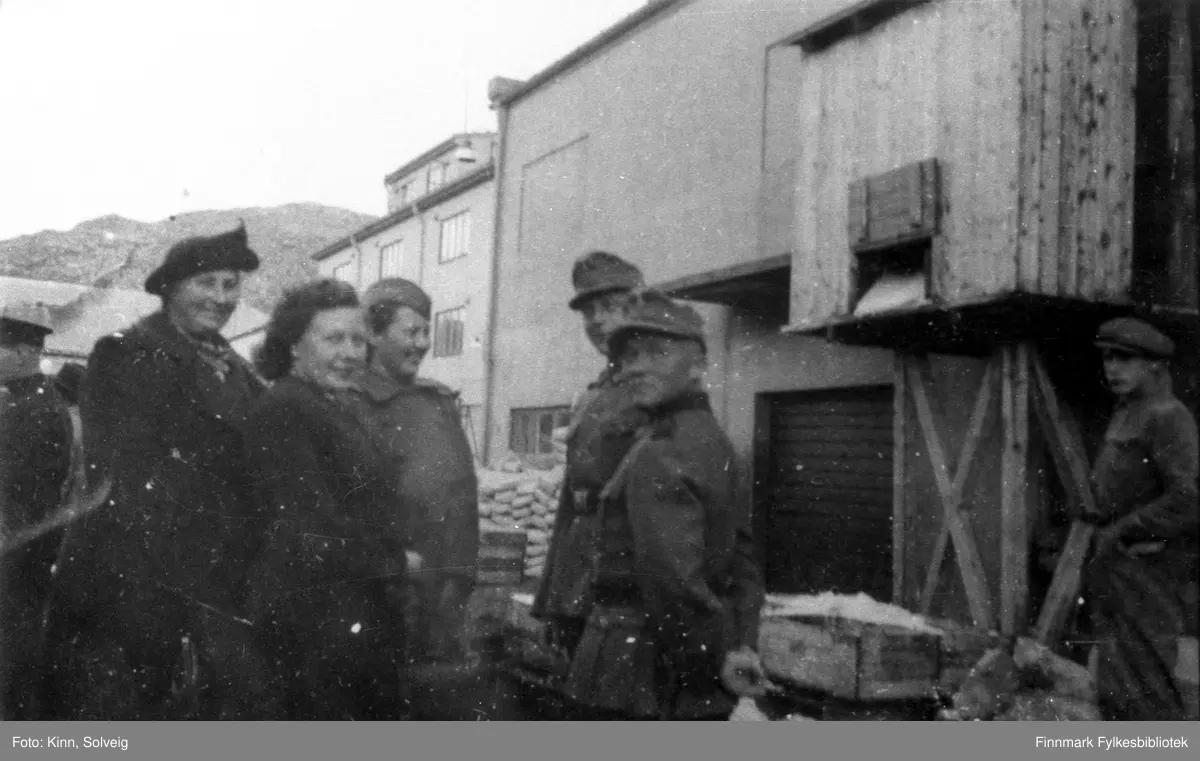Gruppe kvinner ledsaget av tyske soldater i Hammerfest i 1941. Haugens nye gård i bakgrunnen, hvor det tyske sikkerhetspolitiet holdt til.

