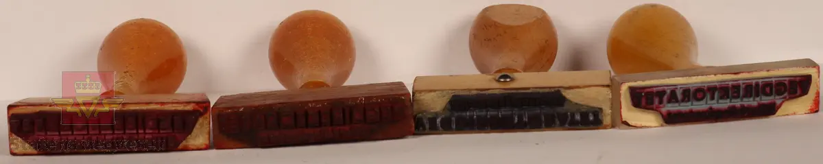 4 Stempler laget av tre som er lakkert. Lyse brun farge. Rektangulære i varierte størrelser med avlangt håndtak. Stempelplatene har fargene blå, rød, rød-brun og grå. Det ene stemplet har overdel som er gjennomsiktig med tekst som viser hva det skal stå på stempelplaten.