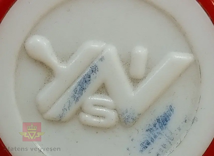 Stempel av plast og stempelplaten er av gummi. Rektangulært stempel med rødt håndtak som er avlangt og som utvider seg. Det er en preget logo på toppen av gjenstand av ukjent navn og opprinnelse.
