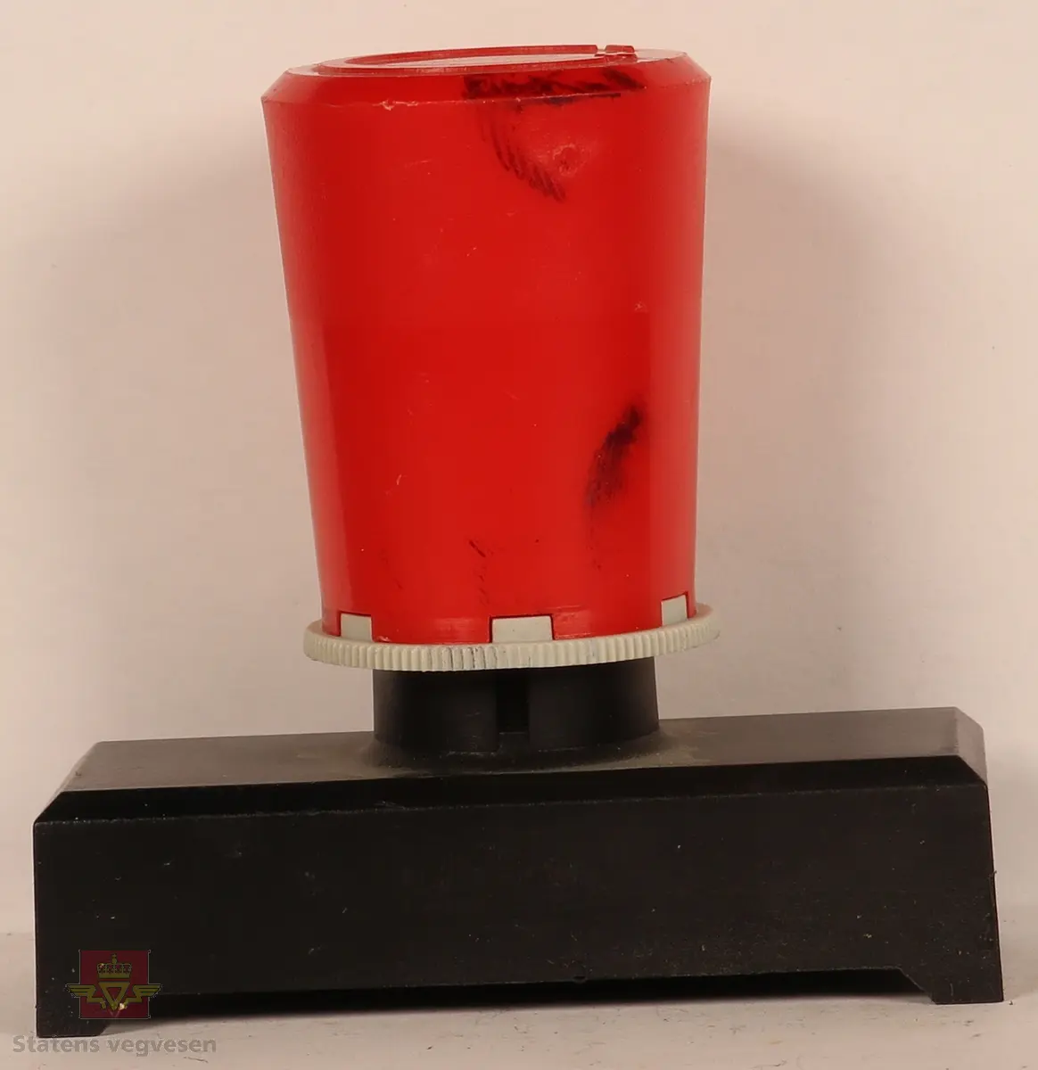 Stempel av plast og stempelplaten er av gummi. Rektangulært, svart stempel med rødt håndtak. På framsiden av stempel står stempel typen i gul skrift. Stempelplaten er blåfarget pga. blekk. 