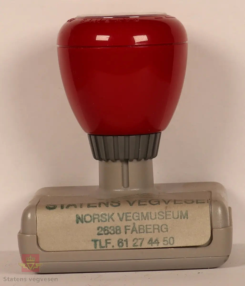 Rødt, grått, hvitt og svart stempel i plast. Firkantet med rundt håndtak. Stempel puten er tørket og har vegvesenets logo med tekst. 