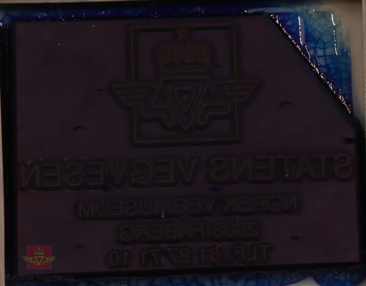Rødt, grått, hvitt og svart stempel i plast. Firkantet med rundt håndtak. Stempel puten er tørket og har vegvesenets logo med tekst. 
